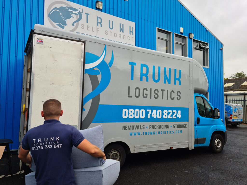 Accreditations & Memberships This image shows the Trunk Self Storage and Trunk Logistics warehouse facility at Unit 54 in Grays, Essex, featuring a lineup of branded low-loader Luton removal vans used for secure storage collections, removals, and logistics services throughout Essex, London, and surrounding regions.