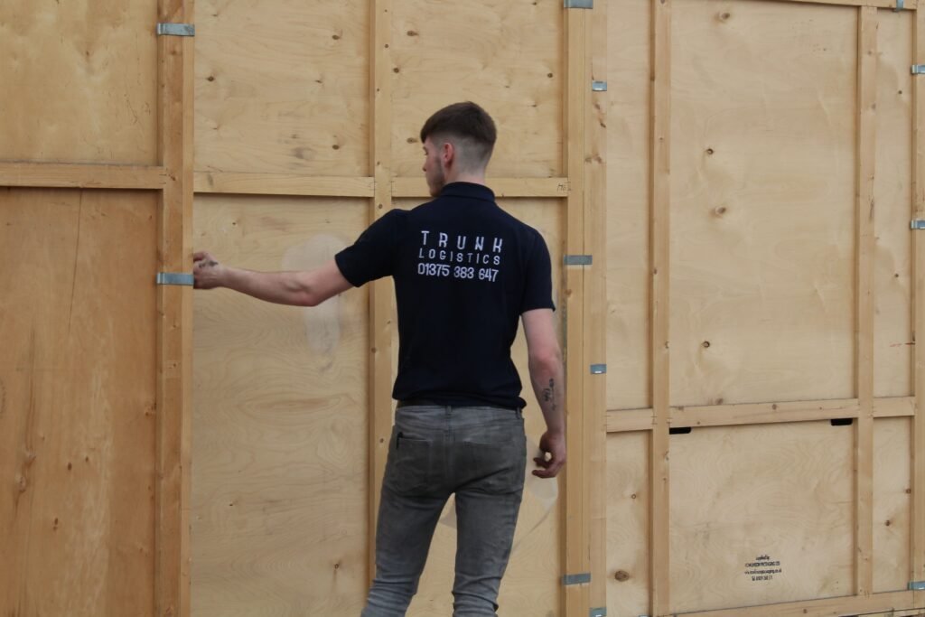 Hotel Clearance and Defit Service Trunk Logistics branded operative inspecting numbered wooden storage crate at commercial warehouse in Grays Essex