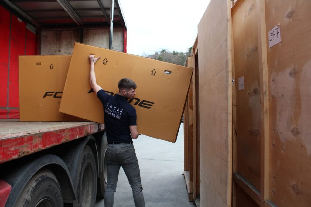 Container to Customer Fulfilment Trunk Logistics operative unloading large Forme bike boxes from delivery vehicle at Grays Essex warehouse
