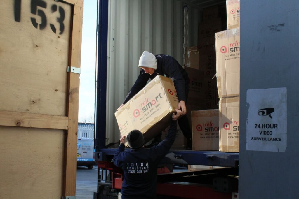 Trunk Logistics team unloading import goods from shipping container at Grays Essex warehouse with 24 hour surveillance signage visible